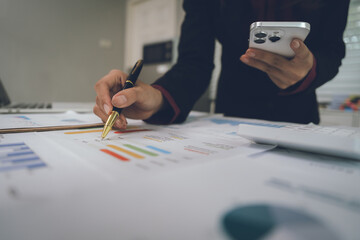 A businesswoman analyzes financial documents with charts and graphs at a desk, highlighting data...