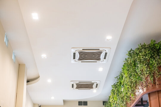 Modern white ceiling with cassette type air conditioner for cool comfort. indoor ventilation system provides clean air and climate control alongside recessed spotlights