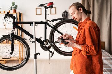 Young man choosing wrench for performing maintenance on bike at home. Concept of fixing and...