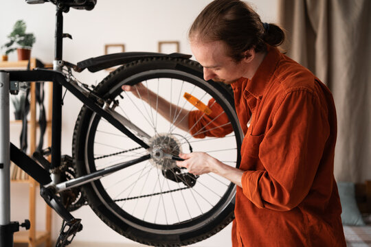 Hipster cyclist repairing bicycle at home tightening wheel with wrench. Bike maintenance and repair concept