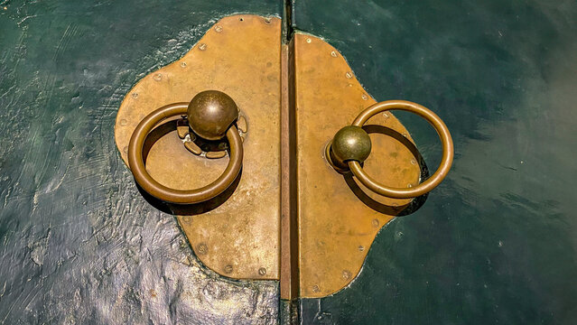 close up of antique gold door handle, antique gold door handles. An antique wooden door with ornamental iron hardware is displayed