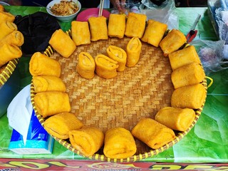 Golden-brown fried spring rolls are neatly arranged in a circular pattern on a woven bamboo tray at...