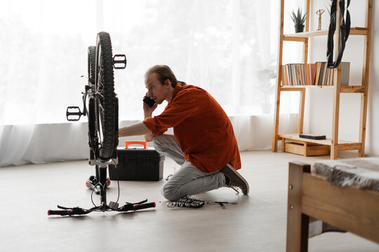 Young man repairing bicycle at home calling support hotline for mechanic consultation. DIY repair concept