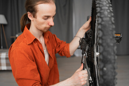Focused man inspects and repairing a bike bicycle in apartment interiors.