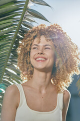 smiling woman with curly hair enjoys sunny tropical background, warm natural light enhancing bright...