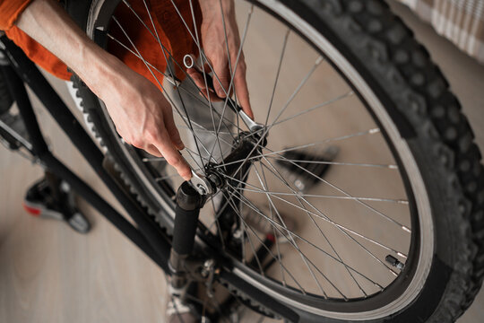 Bike maintenance and repair. Close-up of male hands with wrench to bicycle wheel at home. - Powered by Adobe