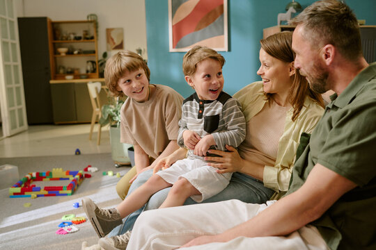 Fototapeta Caucasian middle aged woman and man sitting on sofa interacting with two Caucasian boys, one child and one teenager, smiling and laughing together in home setting with toys visible