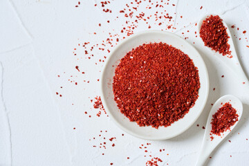 flat lay Korean red chili pepper flake, ground powder coarse paprika or Gochugaru on white table background in spoon and bowl with copy space