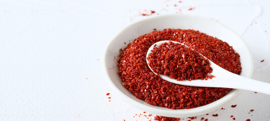 closeup Korean red chili pepper flake, ground powder coarse paprika or Gochugaru on white table background in spoon and bowl with copy space
