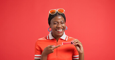 Portrait, lip gloss and black woman in studio, pointing and promotion on red background. African person, makeup and model with cosmetics, announcement and advertising space with beauty and smile