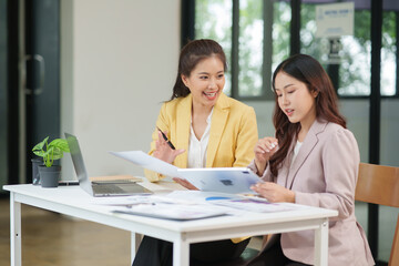 Two Asian businesswomen are sitting in a meeting, planning investment plans, business strategies. On the table are documents and graphs.	