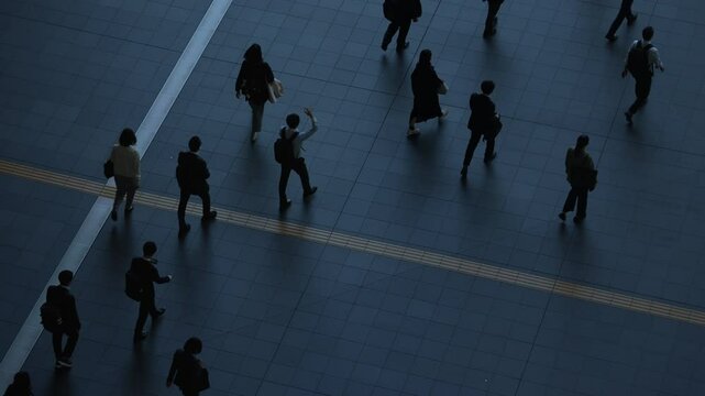 Aerial view of people walking on a tiled floor with strong shadows.
