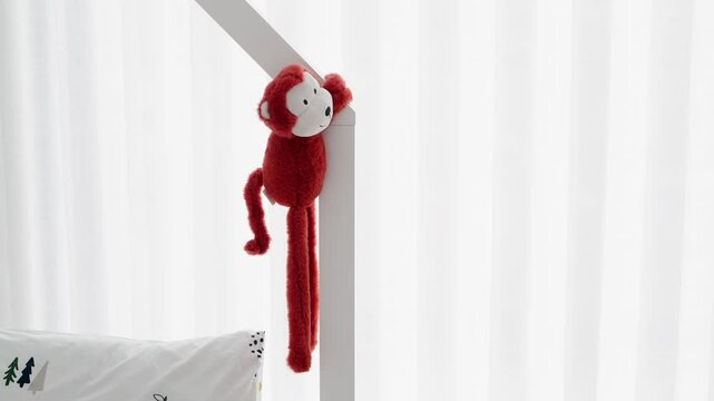 soft red monkey toy wrapped on frame in bright children&rsquo;s bedroom