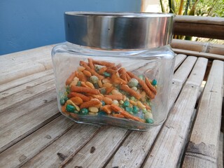 A mix of snacks during Eid such as Bogor peanuts, which taste savory and salty, in a jar on a bamboo chair