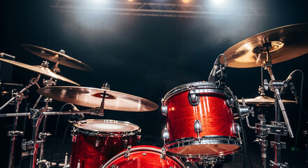 Obraz premium Red Drum Kit on a Concert Stage. A bright red drum kit sits on a dark stage under bright concert lights, ready for a live rock and roll music performance or band rehearsal. 