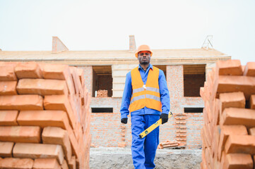 An African American construction worker, in work clothes and a hard hat, is building a brick house