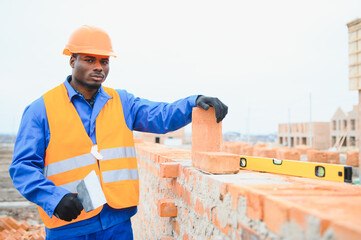 African american Bricklayer industrial worker installing brick masonry on exterior wall with trowel...