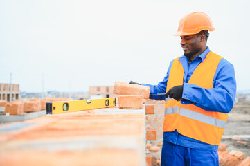 Builder in workwear and protective helmet keeping level handtool on surgace of brick layer while...