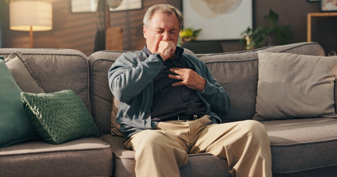 Senior, sick man and couch with chest pain on sofa for cardiac arrest or bronchitis at home. Elderly, male person or patient with illness, virus or viral infection for lung disease or heart attack