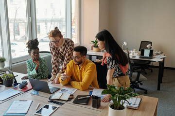 Gen Z diverse people collaborating around desk with laptop and documents in modern coworking...