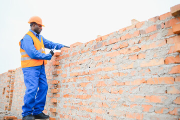 African american Bricklayer industrial worker installing brick masonry on exterior wall with trowel...