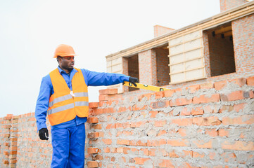 African american construction worker. Portrait of mason bricklayer installing red brick with trowel...