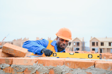 Builder in workwear and protective helmet keeping level handtool on surgace of brick layer while...