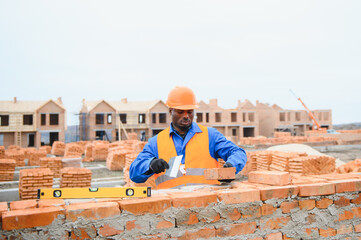 African american construction worker. Portrait of mason bricklayer installing red brick with trowel...