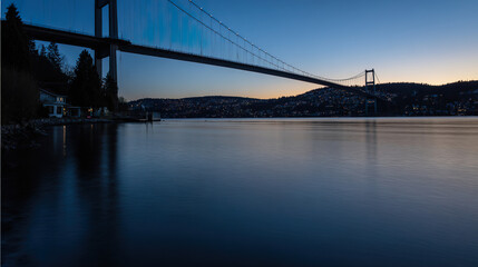 Obraz premium Suspension bridge in twilight, reflections on water, long exposure. Urban serenity meets timeless structure.