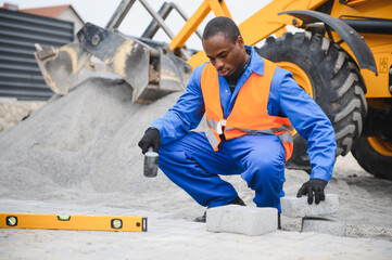 African american master in gloves lays paving stones in layers. Laying gray concrete paving slabs...