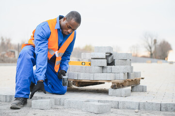African american master in gloves lays paving stones in layers. Garden brick pathway paving by...