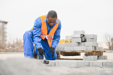 African american master in gloves lays paving stones in layers. Laying gray concrete paving slabs...