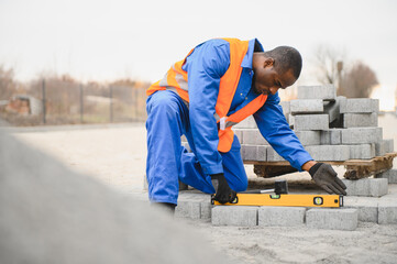 African american master in gloves lays paving stones in layers. Laying gray concrete paving slabs...