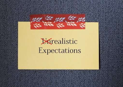 stick note written - Unrealistic expectations - expectations that are set highly improbable or unattainable - lead us to disappointment unhappiness and dissatisfaction