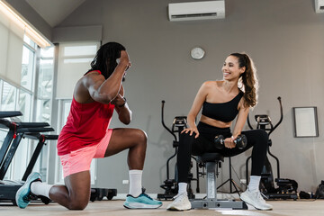 A man and a woman are in a gym. The man is squatting down and the woman is sitting on a bench