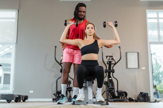 A man and a woman are working out together. The man is lifting weights while the woman is watching