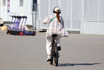 A woman rides a bicycle down a street with a backpack on her back