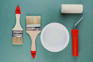 Flat lay of paintbrushes, roller and white paint bucket on green background for interior decoration...