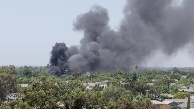Drone footage of dense black smoke rising above homes in a suburban neighborhood during the early stages of a fire. No flames visible, but smoke indicates active emergency.