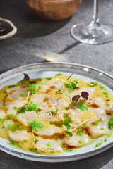 Scallop carpaccio with citrus sauce in bright rustic lighting, closeup restaurant plating
