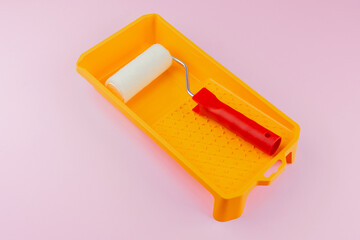 Red handled roller in yellow tray on pink background for home painting and renovation concept