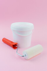 Paint roller and white bucket on pink background for home renovation and painting supply concept