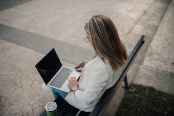 Businesswoman working on laptop outdoors on bench
