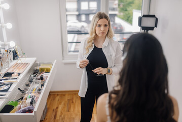 Makeup artist holding eyebrow pencil and looking at client in beauty salon