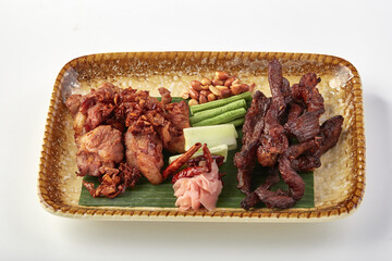 Crispy fried fermented pork ribs and sun dried beef served on ceramic plate with fresh vegetables, peanuts, and pickled ginger, creating flavorful and appetizing dish