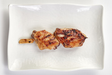 Grilled chicken wings on skewer served on white rectangular plate, showcasing golden brown charred texture and juicy appearance, perfect for delicious meal