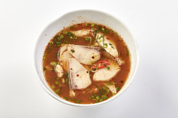Spicy fish soup with fresh herbs, chili, and flavorful broth served in white bowl, showcasing traditional and aromatic dish