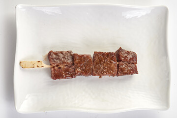 Grilled beef skewer served on white ceramic plate, showcasing juicy, tender meat with glossy glaze....