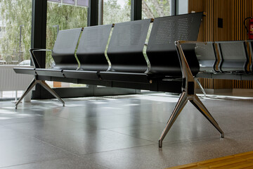 Empty metal bench seats in a public waiting area, minimalistic interior, polished floor, and wooden wall panels, concept of transportation hub, hospital, government office waiting room. Bus station