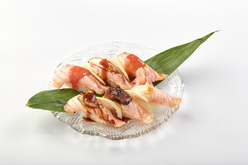 Grilled salmon sushi with glossy sauce, garnished with lemon slices and served on clear glass plate with green leaf for decoration, creating fresh and appetizing presentation